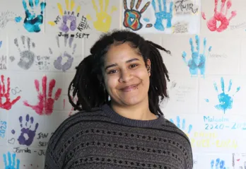Y youth housing client Ica standing and smiling in front of a wall covered in colourful handprints