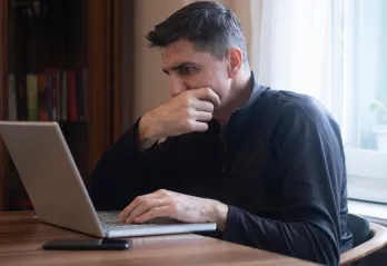 A man looking at a laptop screen with a stressed expression