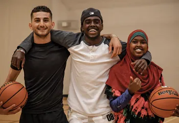 Three young adults playing basketball in the gymnasium.