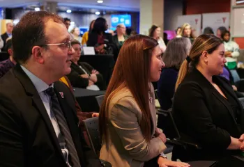 Andrew, Katie, and Cass from the YMCA leadership team sitting in a crowd of people