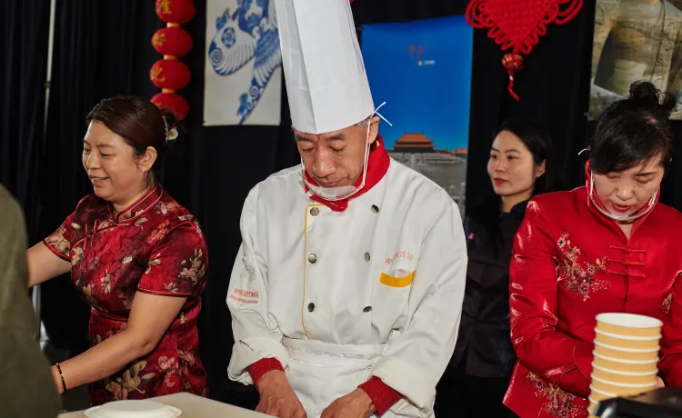 A chef and three other people preparing and serving food at the Chinese food booth.