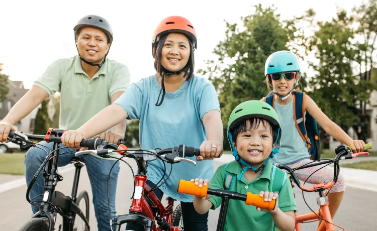 A happy family of four wearing helmets are biking outdoors.