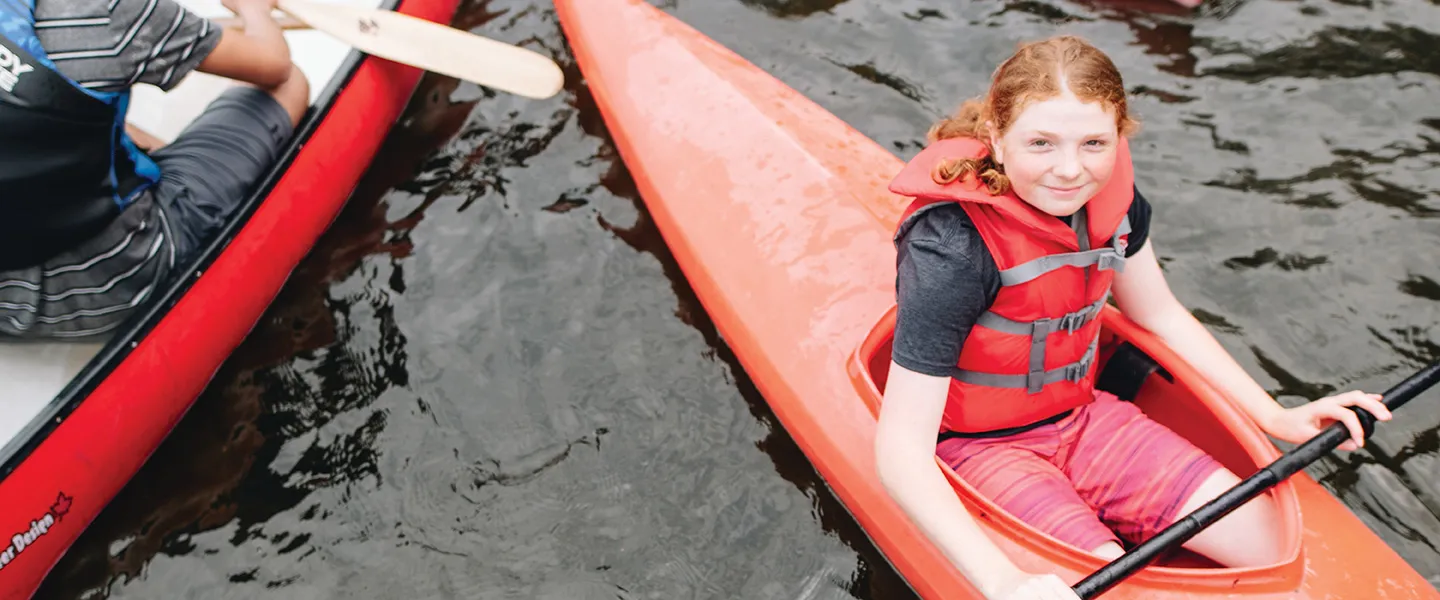 A girl with red hair sits in a red kayak.