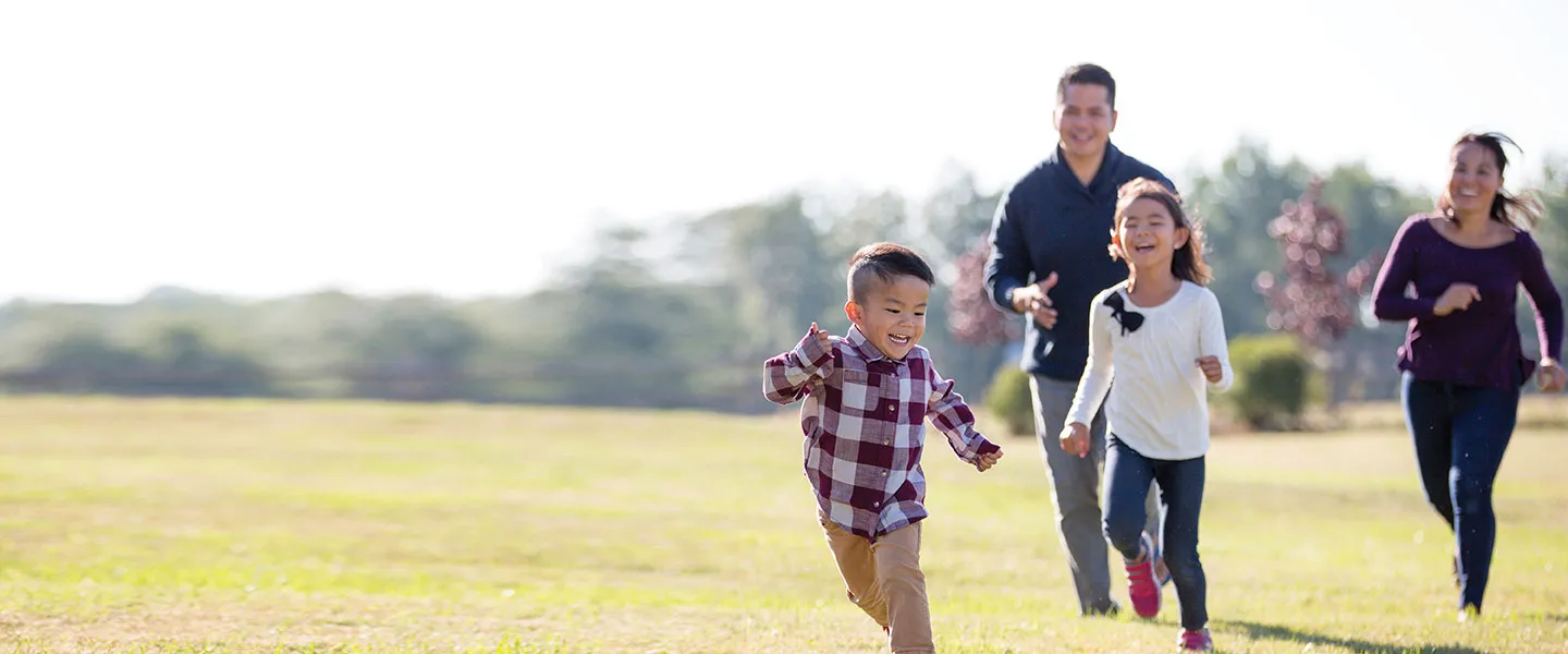 A family joyfully running together in a green field under a clear blue sky.