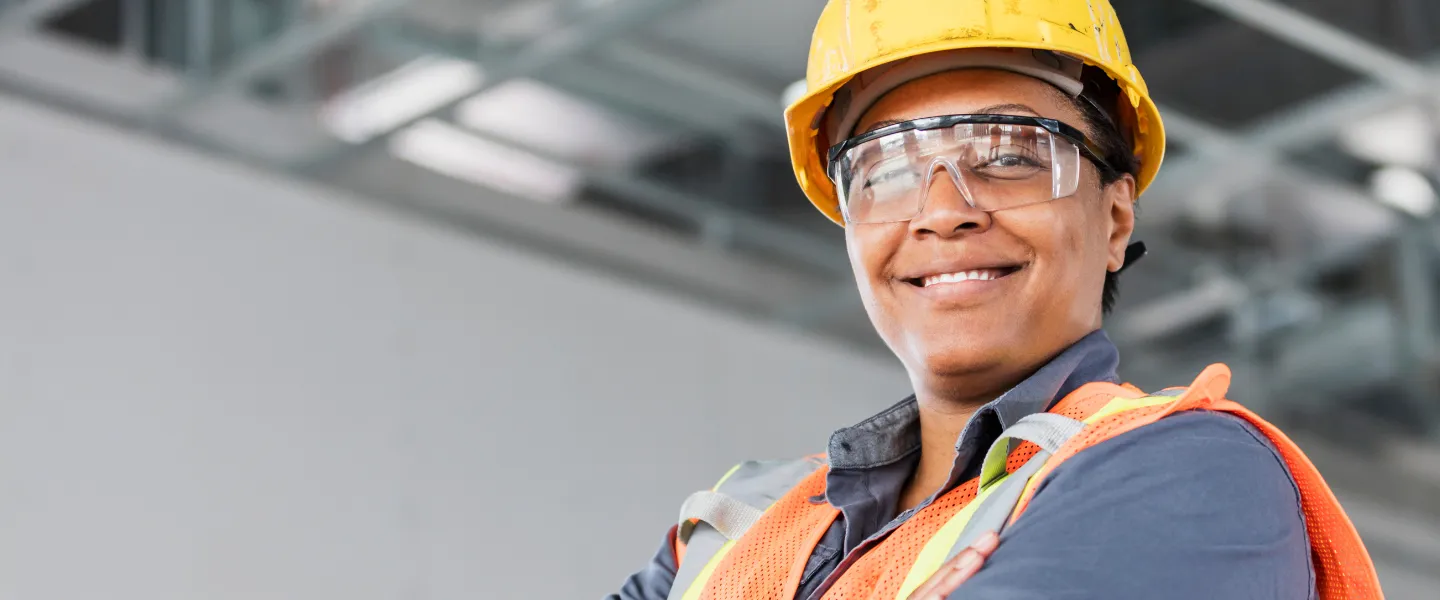 A woman smiling and crossing her arms. She is wearing construction attire.