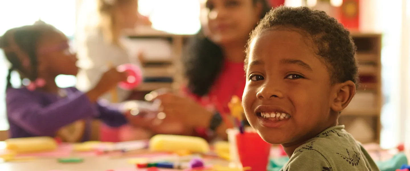 A happy child seated at a table with other children, all engaged in a joyful and friendly atmosphere.