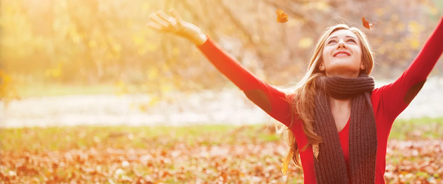 A woman in a red sweater raises her hands in the air, expressing joy.
