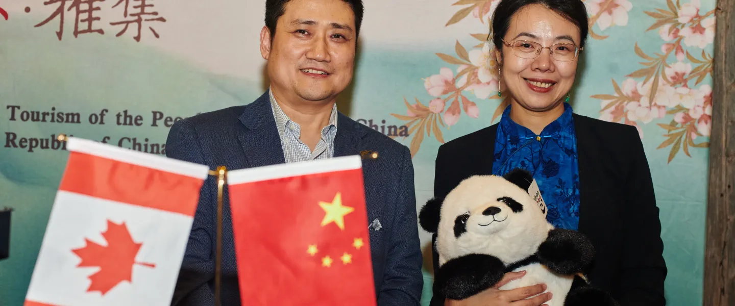 Two people standing at a Chinese cultural booth. One is holding a plush panda. In front of them are the Canadian and Chinese flags.