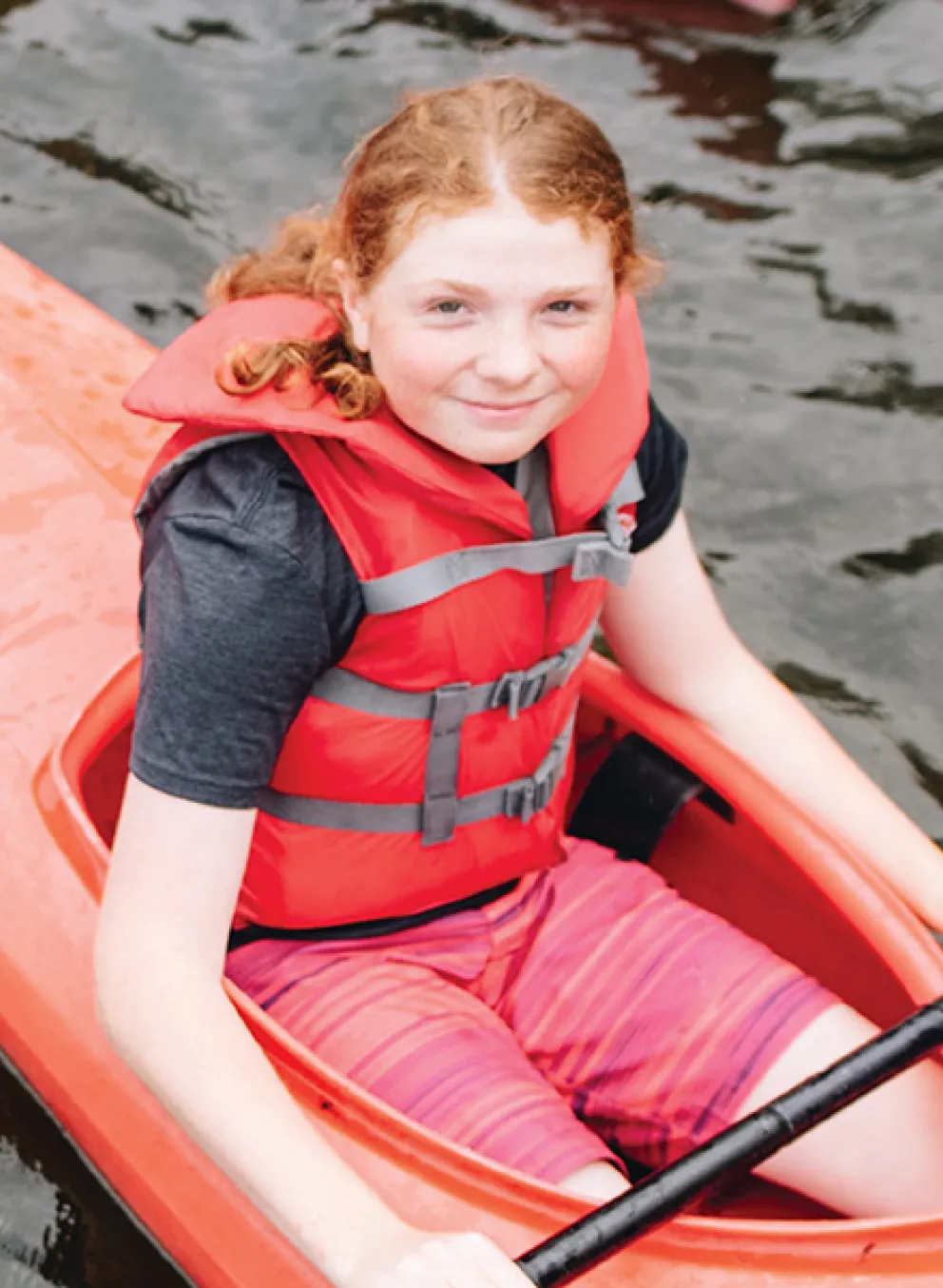 A girl with red hair sits in a red kayak.