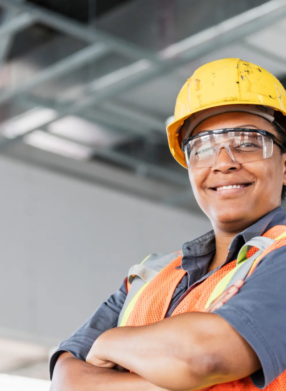 A woman smiling and crossing her arms. She is wearing construction attire.