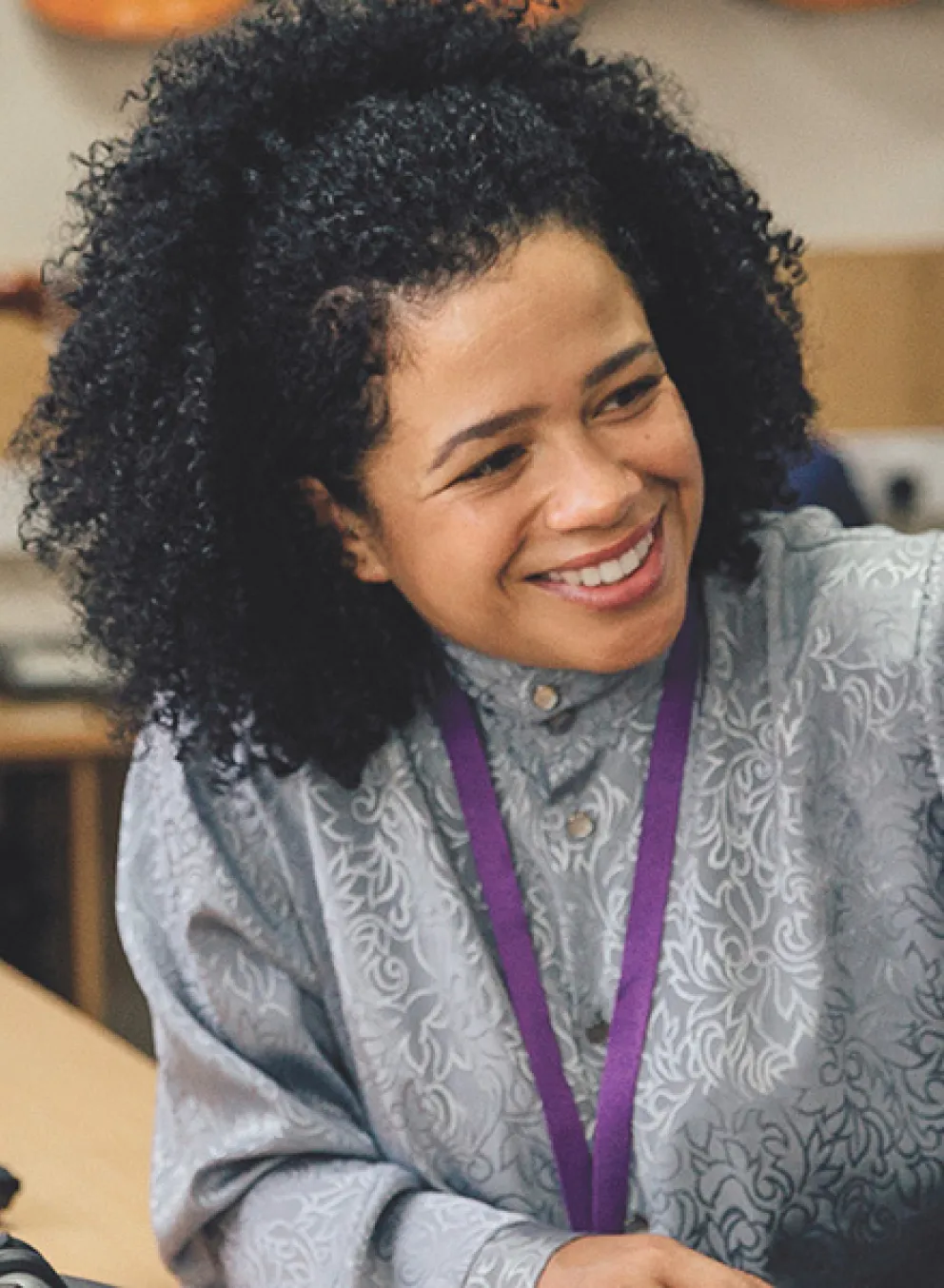A young girl wearing headphones engages in conversation with her teacher in a classroom setting.