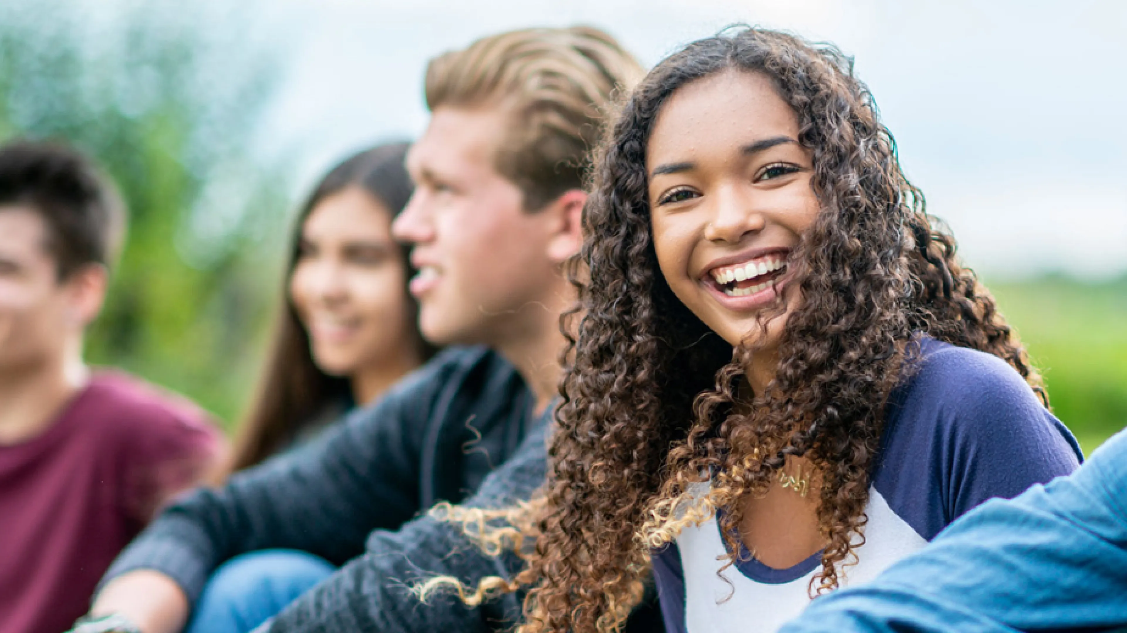A diverse group of smiling young people sitting together outside.