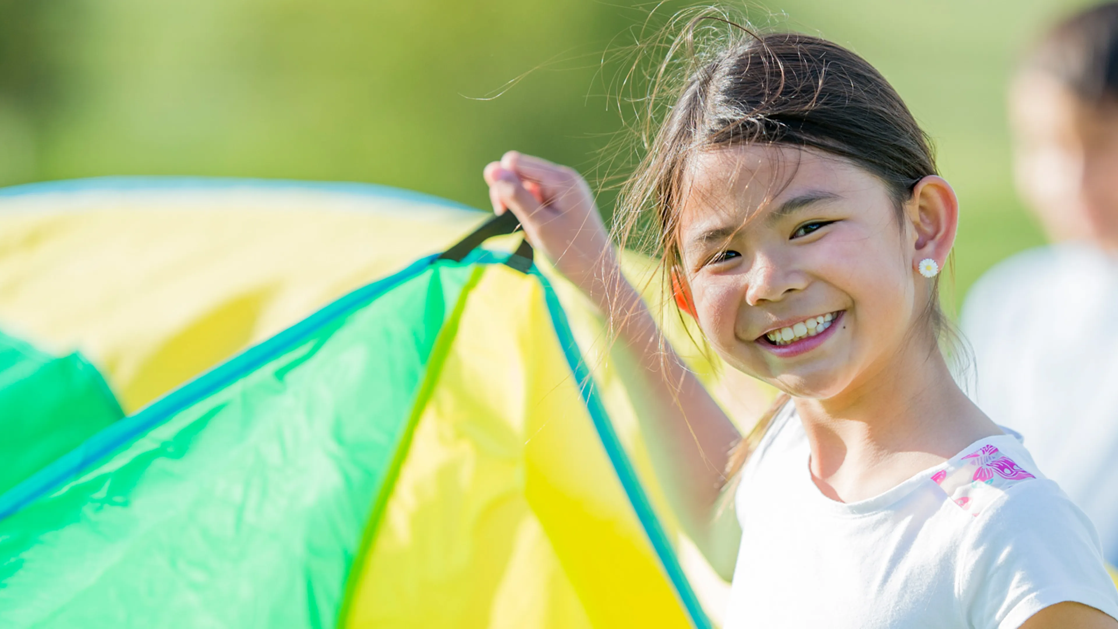 A girl holding up a section of a parachute participates in outdoor camp activities.