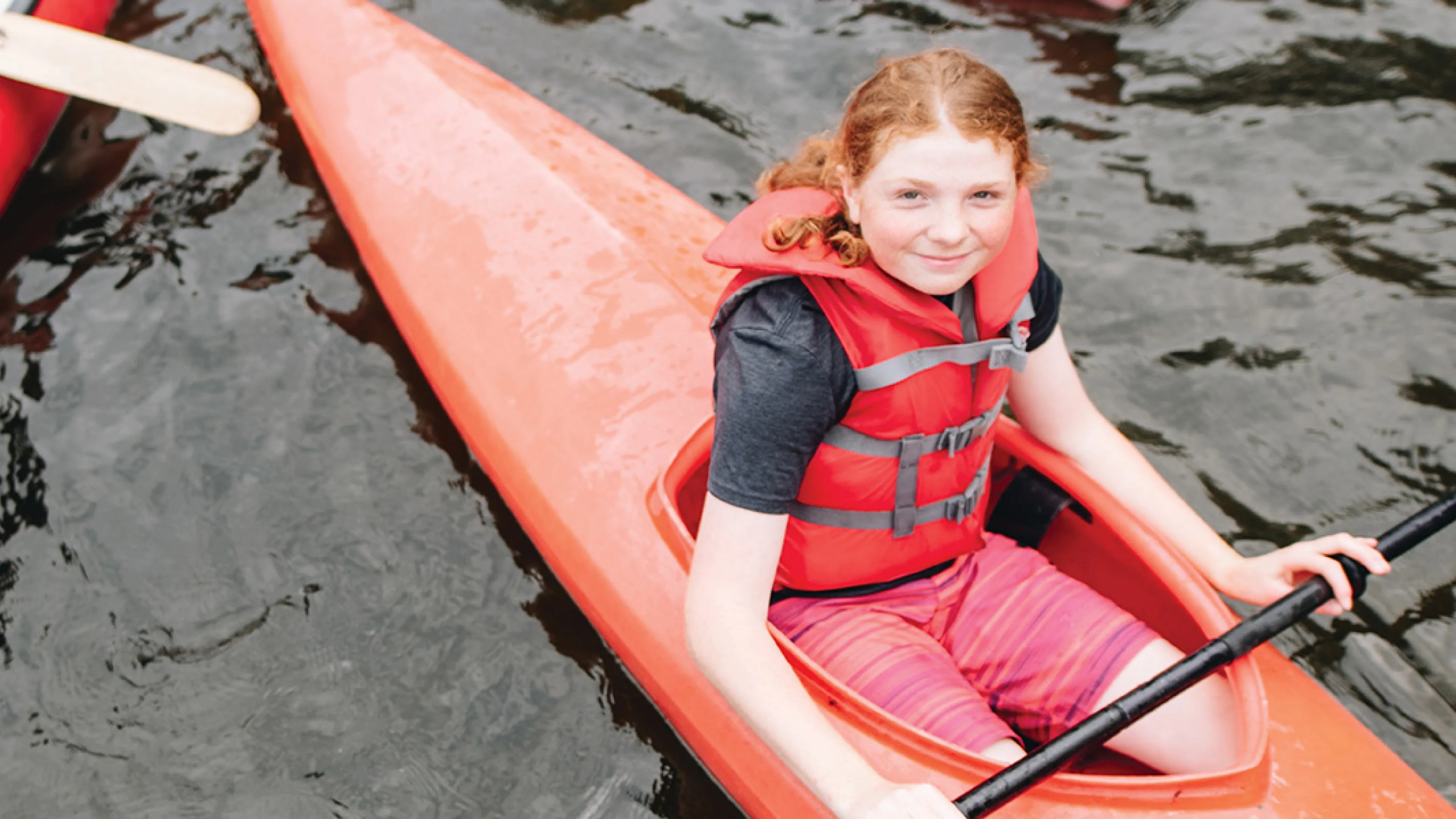 A girl with red hair sits in a red kayak.