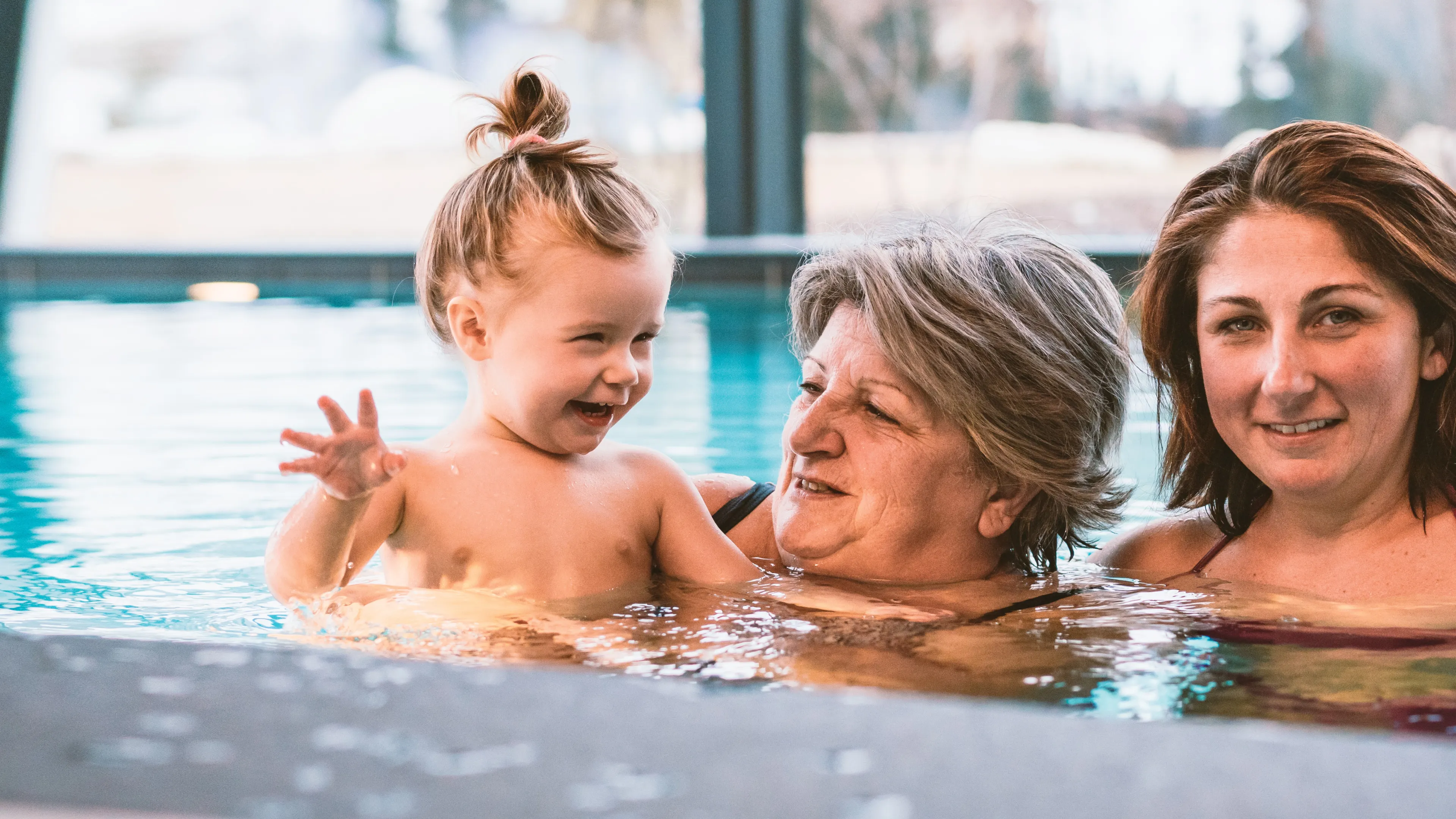 Three generations of family members play together in an indoor swimming pool