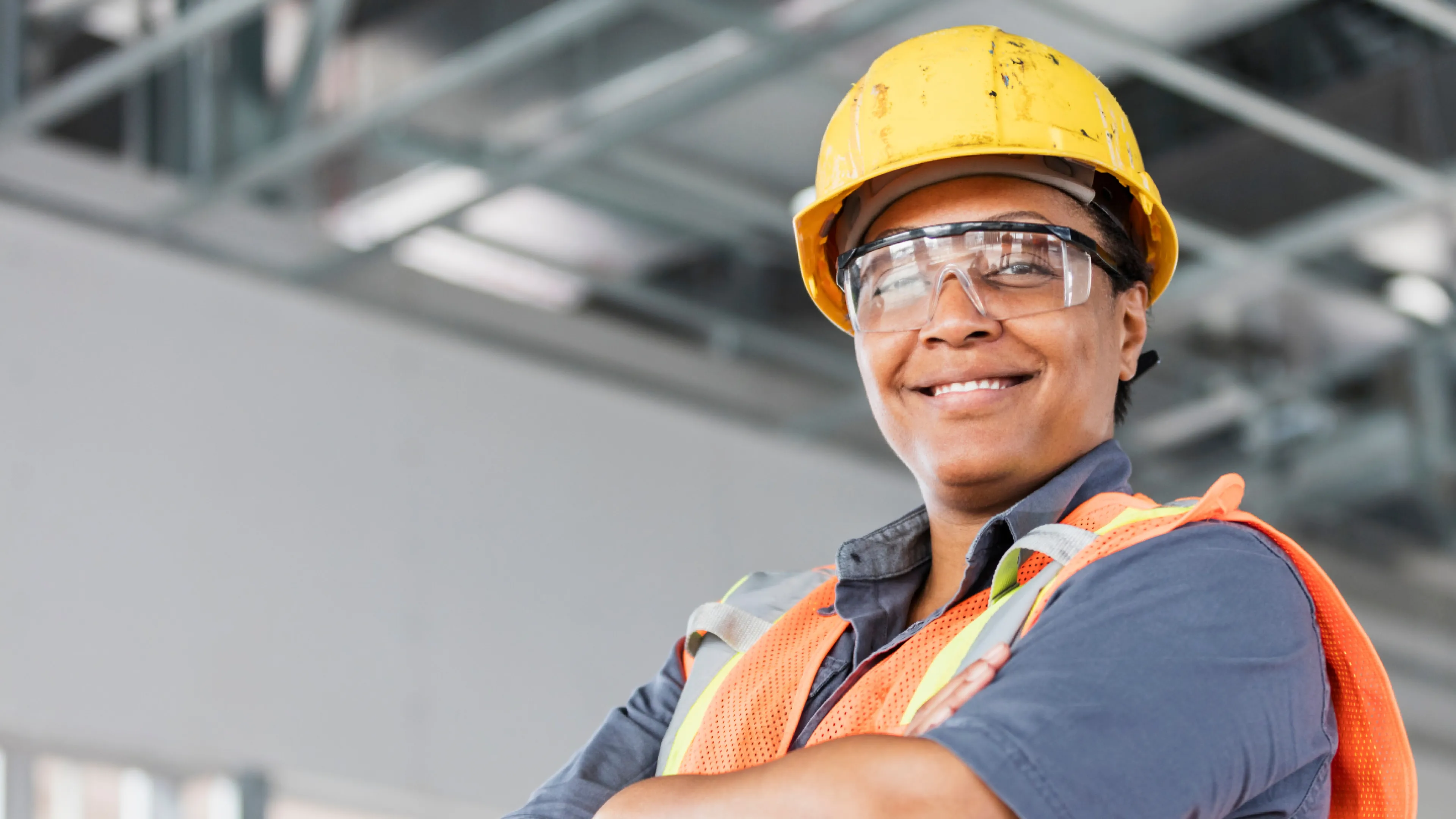 A woman smiling and crossing her arms. She is wearing construction attire.