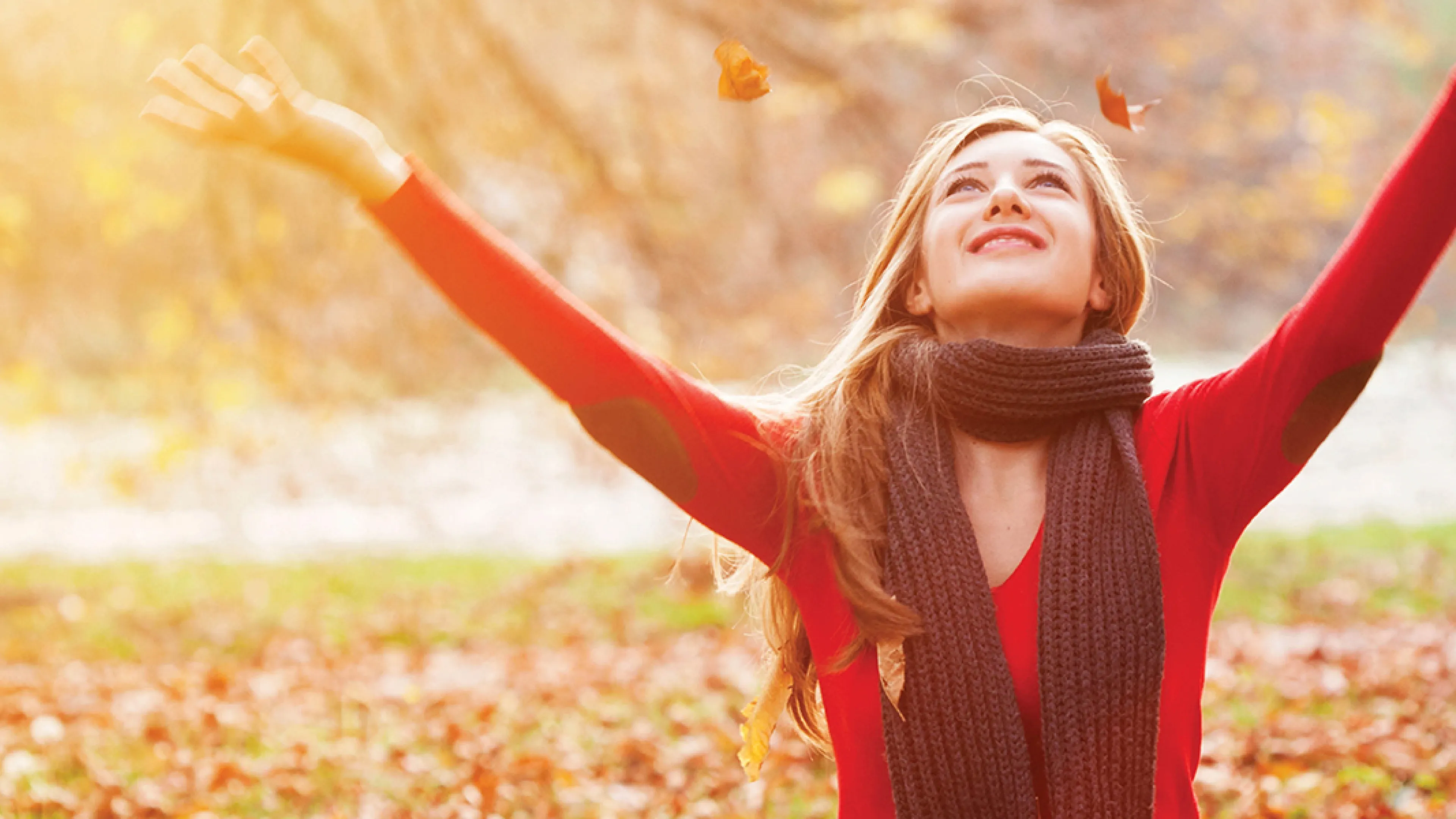 A woman in a red sweater raises her hands in the air, expressing joy.