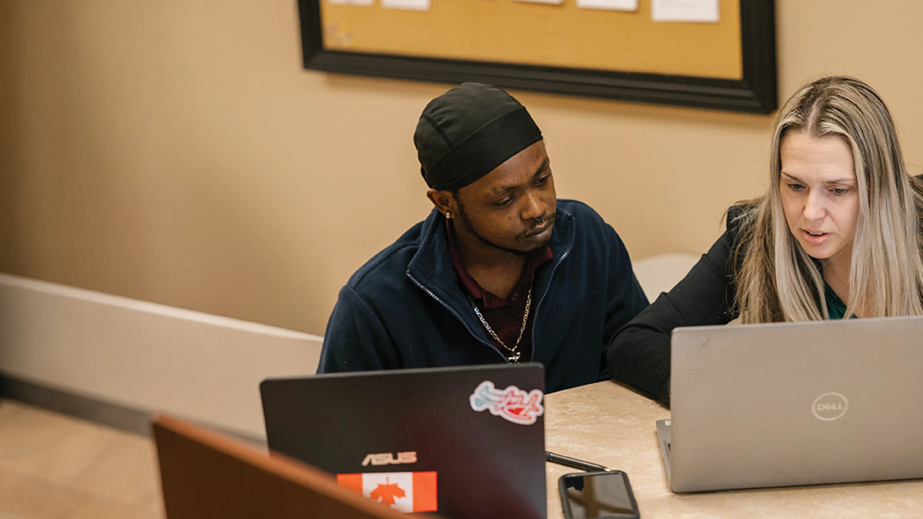 Two individuals focused on their laptops while collaborating in a modern office setting.