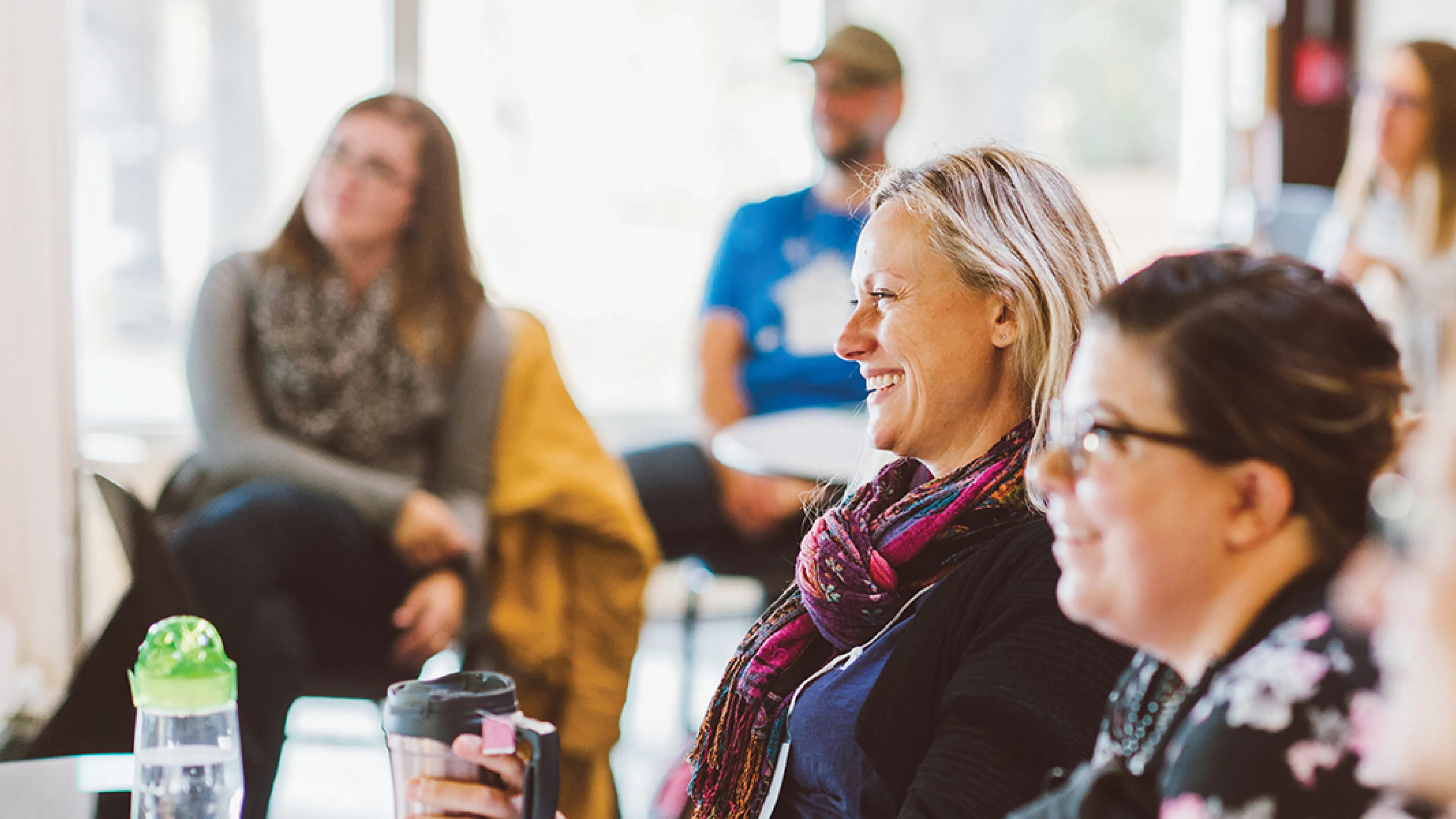 A diverse group of people sitting at tables in a bright room, smiling and engaged