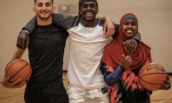 Three young adults playing basketball in the gymnasium.