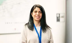 A woman with long black hair, smiling softly while facing the viewer.