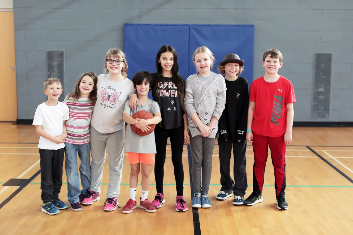 A group of children standing in a gymnasium. One is holding a basketball.