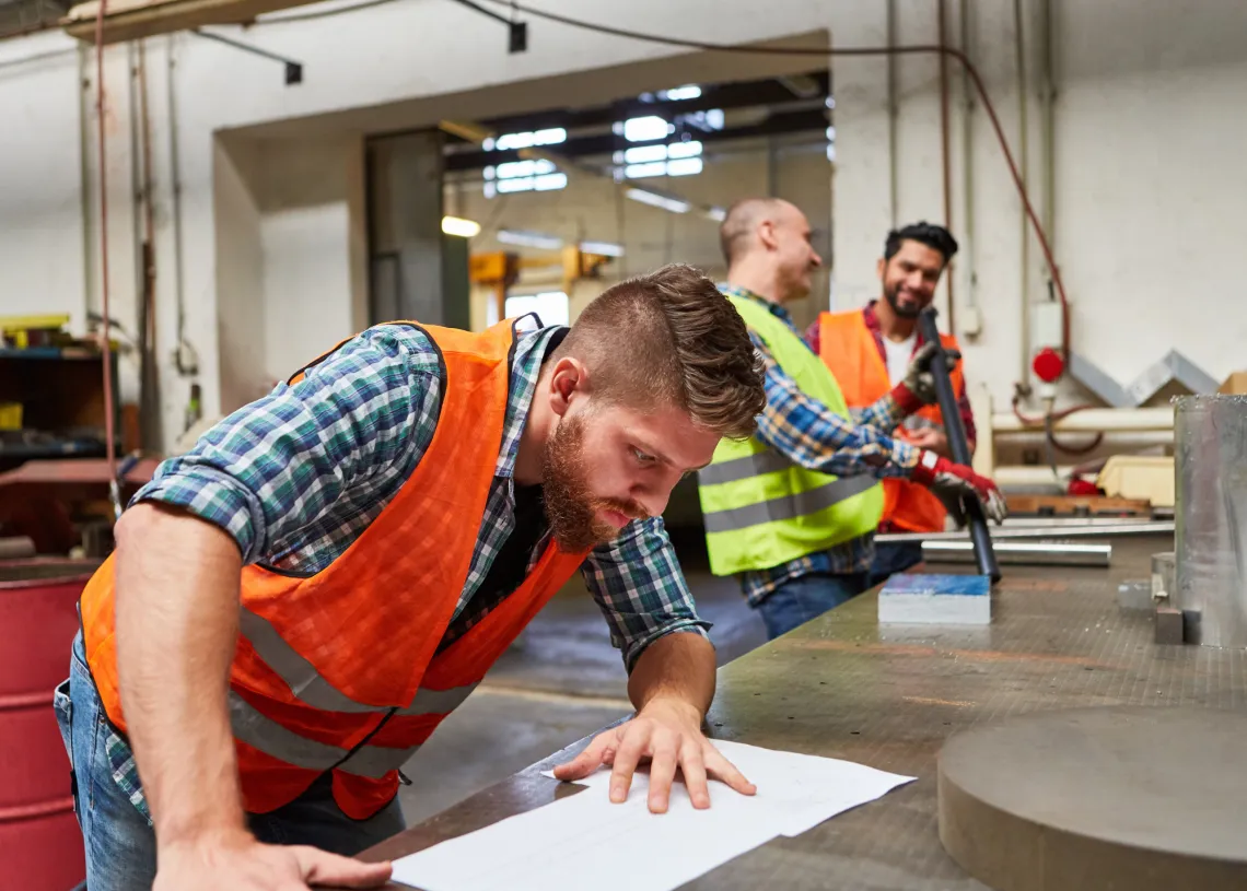 Three men at a worktable, wearing construction vests