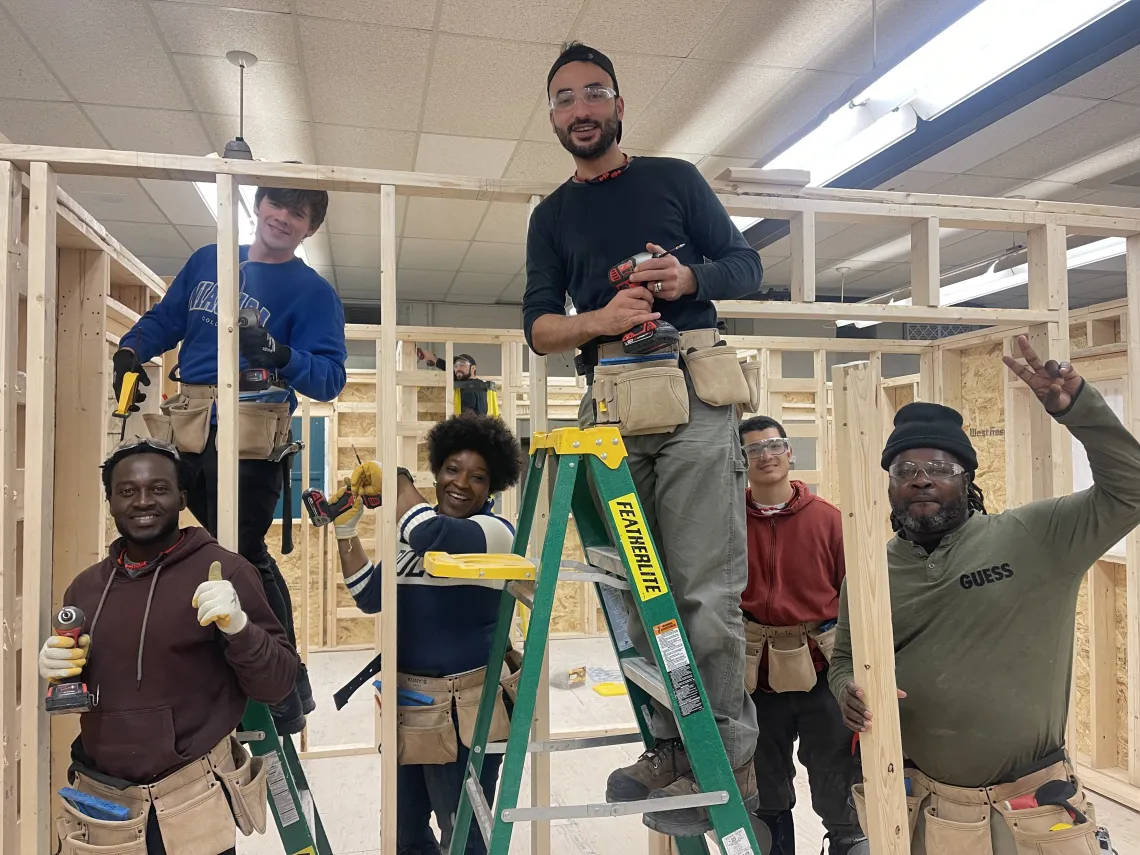 Six skilled trades program participants in a workshop, building a wooden structure framework