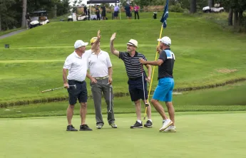 Four golfers on a golf course, two of them are high fiving