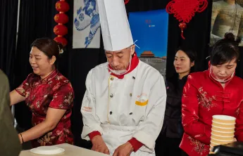 A chef and three other people preparing and serving food at the Chinese food booth.