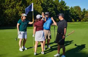 Four golfers high fiving on a golf course