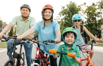 A happy family of four wearing helmets are biking outdoors.