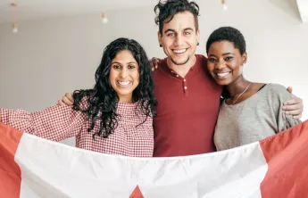 A man and two women, all of different cultural backgrounds, smiling and holding up a Canadian flag together