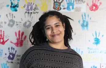 Y youth housing client Ica standing and smiling in front of a wall covered in colourful handprints