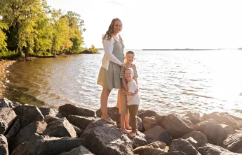 Lindsey standing with her two sons on rocks by a lake