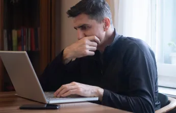 A man looking at a laptop screen with a stressed expression