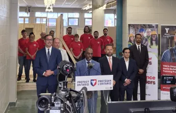 A group of people including Trevor McAlmont, Minister Piccini, and YMCA Power of Trades staff standing in front of a camera.
