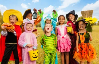 Eight children in various Halloween costumes posing in a field