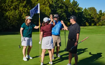 Four golfers high fiving on a golf course