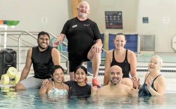 A group of people smiling and posing together in a pool for a photo, showcasing a fun and lively atmosphere.