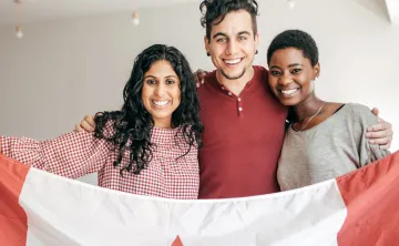 A man and two women, all of different cultural backgrounds, smiling and holding up a Canadian flag together