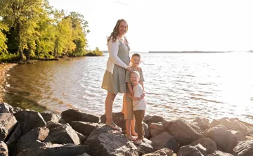 Lindsey standing with her two sons on rocks by a lake