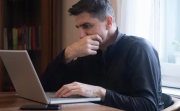 A man looking at a laptop screen with a stressed expression