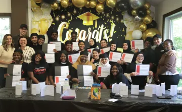 The graduating class of the YMCA's Culinary Training Program standing alongside program staff and holding their certificates